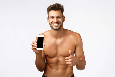 Musculine handsome shirtless bodybuilder, smiling happy, recommend smartphone application, promote product on mobile page, show thumbs-up, like or approve, give advice call fitness instructorの写真素材