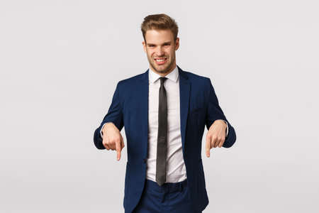 Guy turn your attention at something awful and unpleasant. Attractive blond bearded businessman in classic suit, pointing down and grimacing from aversion, seeing creepy thing, white backgroundの写真素材