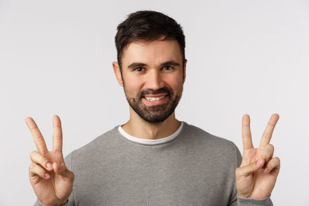 Close-up studio shot friendly, outgoing and optimistic handsome bearded male in grey sweater, show...