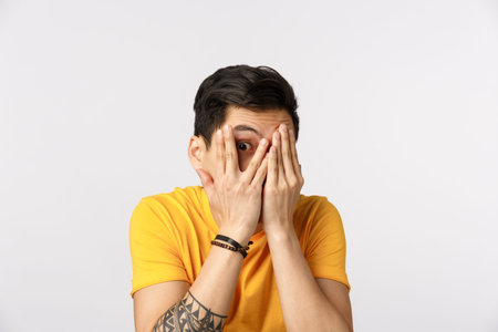 Scared but curious cute asian man with short dark hair, tattoos, hiding face, close eyes with hands...
