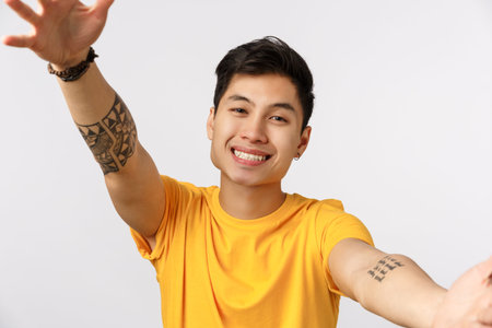 Close-up shot tender charming young millennial asian guy in yellow t-shirt, spread hands in cuddle,...