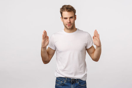 Handsome stylish blond bearded macho man in white t-shirt, raising hands near chest as if holding...
