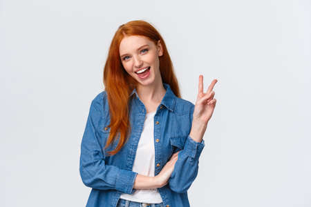 Business, university and people concept. Attractive cheerful redhead woman in denim shirt, send positivity and happiness, showing peace sign and smiling carefree, standing white backgroundの写真素材