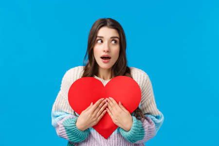 Waist-up portrait surprised and curious wondered caucasian woman dont know who prepared valentines-day gift for her, looking around open mouth amazed, embracing cute red cardboard heartの写真素材