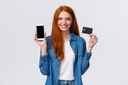 Waist-up portrait confident female with red long hair, blue eyes, holding credit card and showing...