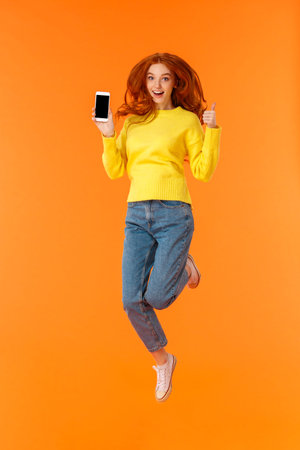 Advertising, technology and holidays concept. Vertical full-length shot cheerful gorgeous ginger...