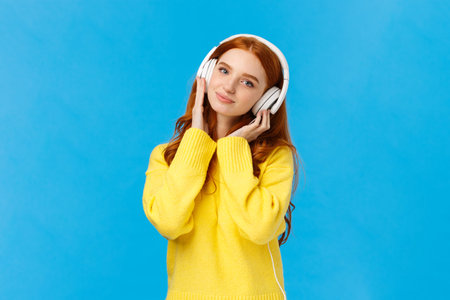 Waist-up shot tender and cute, lovely redhread woman in yellow sweater, tilt head, wear headphones,...