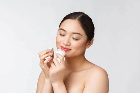 Beautiful young woman on white isolated background holding cosmetic face cream, asianの写真素材