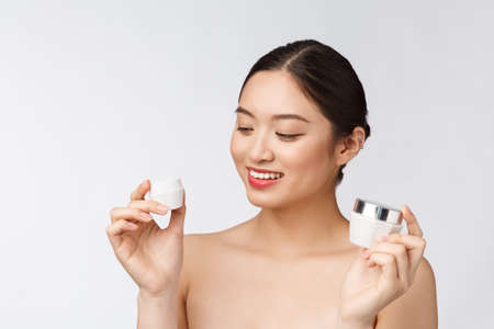 Beautiful young woman on white isolated background holding cosmetic face cream, asianの写真素材