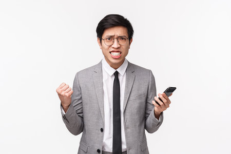 Waist-up portrait of displeased, bothered and annoyed asian businessman in grey suit, clenching...