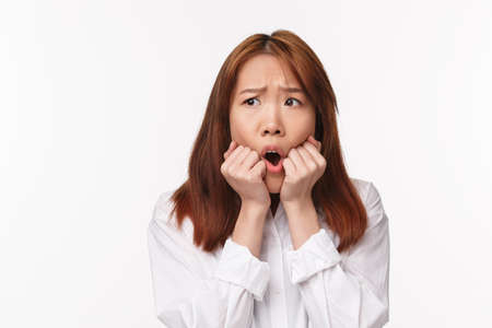 Close-up portrait of asian girl in panic, look afraid and concerned, look away trembling fear, biting fingers and grimacing, having huge trouble, being alarmed or anxious, stand white backgroundの写真素材