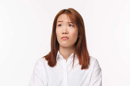 Close-up portrait of skeptical young asian girl grimacing aversion and judgemental looking left, raising eyebrow surprised and unimpressed with something unpleasant, stand white backgroundの写真素材