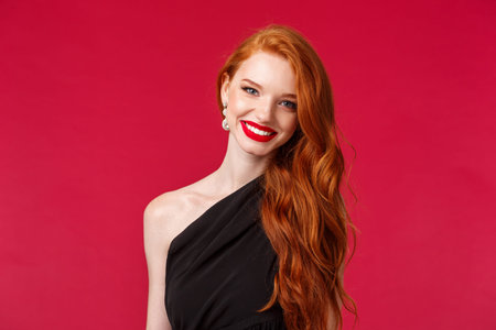 Makeup, beauty and women concept. Close-up of elegant pretty redhead woman in luxurious slim black dress, red lipstick, smiling cheerful and pleased, attend formal event, party or romantic dateの写真素材