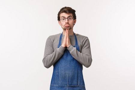 Portrait of pleading cute silly caucasian man in apron, coffee shop employee asking coworker cover...