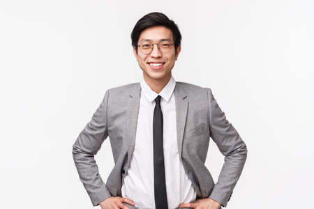 Lets earn some money. Handsome confident and smart asian businessman in suit and tie, standing in ready, determined pose, smiling upbeat, assured he will get deal, white backgroundの写真素材