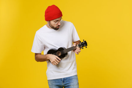 Young handsome guitar player. Studio shot on yellow background.
