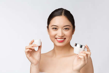 Beautiful young woman on white isolated background holding cosmetic face cream, asianの写真素材