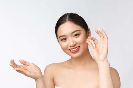 Young attractive asian woman who takes a capsule or pill. Isolated over white background.の写真素材