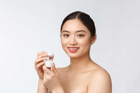 Beautiful young woman on white isolated background holding cosmetic face cream, asianの写真素材