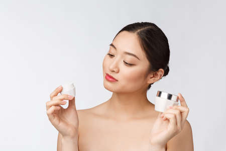Beautiful young woman on white isolated background holding cosmetic face cream, asianの写真素材
