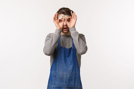 Portrait of shocked and astonished young man in apron, coffee shop worker rub eyes from disbelief,...
