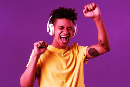Close-up portrait of cheerful, happy young dancing guy lift hand up singing along, close eyes and...