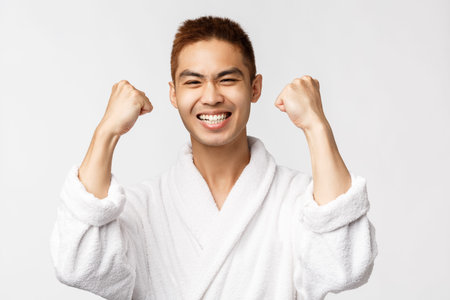Beauty, spa and leisure concept. Satisfied asian man in bathrobe fist pump delighted, smiling...