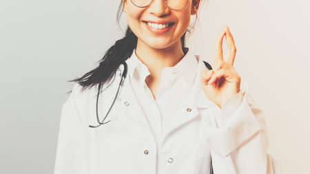 Close-up portrait of enthusiastic, smiling attractive asian female doctor, therapist check-up child in hospital, showing few tricks to cheer patient, standing upbeat grey backgroundの写真素材