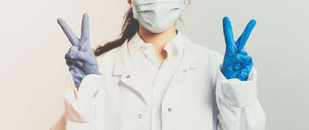 Covid19, coronavirus, healthcare and doctors concept. Portrait of optimistic asian female doctor ask to stay safe, wear medical mask and gloves, show peace sign, hope we defeat virus pandemiaの写真素材