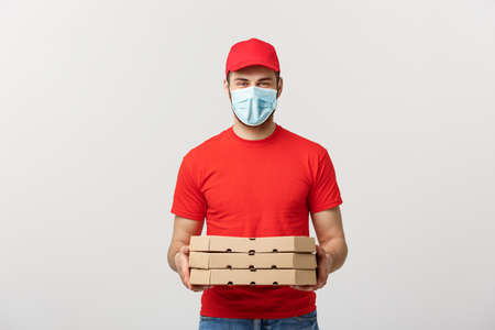 Online delivery and Coronavirus Concept. Cheerful young deliveryman in face mask holding pizza boxes while isolated on white studio backgroundの写真素材