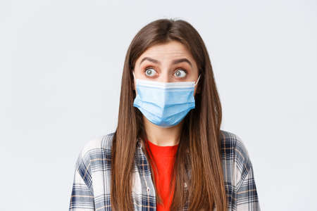 Coronavirus outbreak, leisure on quarantine, social distancing and emotions concept. Close-up of surprised caucasian woman in casual clothes and medical mask, staring left speechlessの写真素材