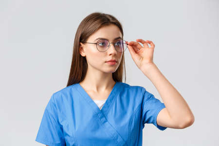 Healthcare workers, medicine, insurance and covid-19 pandemic concept. Professional young smart doctor or nurse, female intern in scrubs and glasses, looking right at banner serious faceの写真素材