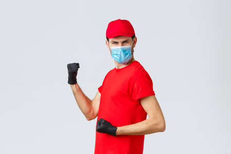 Covid-19, self-quarantine, online shopping and shipping concept. Energized, excited delivery guy do champion dance, fist pump and looking empowered, celebrate success, rejoicing in courier outfitの写真素材