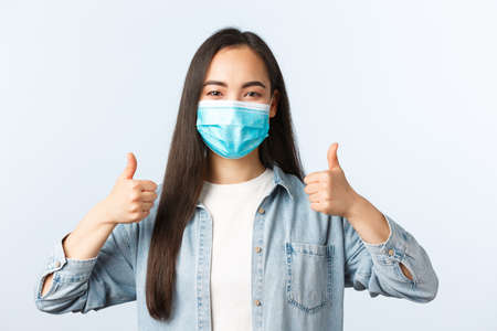 Social distancing lifestyle, covid-19 pandemic everyday life and leisure concept. Supportive enthusiastic asian woman in medical mask thumbs-up, wearing PPE while going grocery shoppingの写真素材