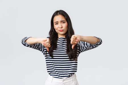 Lifestyle, beauty and fashion, people emotions concept. Judgemental disappointed asian woman showing negative opinion, make thumbs-down and smirk unsatisfied, rating bad productの写真素材