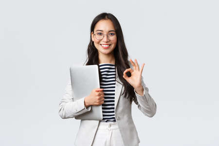 Business, finance and employment, female successful entrepreneurs concept. Young confident businesswoman in glasses, showing okay gesture, hold laptop, guarantee best service qualityの写真素材