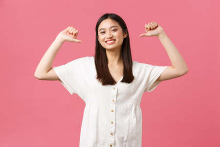 Beauty, people emotions and summer leisure and vacation concept. Proud happy korean girl show-off, smiling proud and pointing at herself with pleased expression, pink backgroundの写真素材