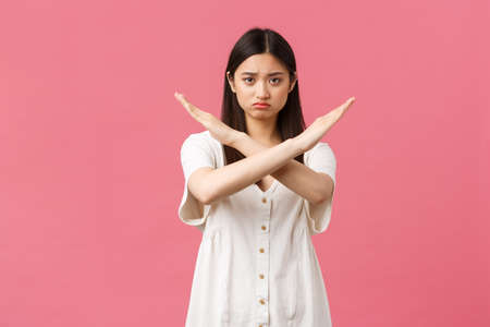 Beauty, people emotions and summer leisure concept. Serious insecure and timid gloomy asian girl asking stop, making cross sign, fed up with bullying, forbid such behaviour, pink backgroundの写真素材
