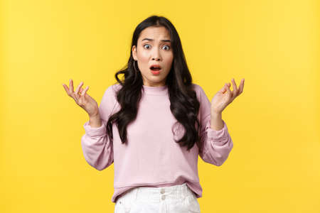 People emotions, lifestyle and fashion concept. Shocked asian woman in panic, looking frustrated and alarmed as hear bad news, raising hands in dismay, got in trouble, yellow backgroundの写真素材