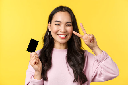 People emotions, lifestyle leisure and beauty concept. Close-up of cheerful smiling asian woman showing credit card and peace sign, recommend paying online, shopping for summerの写真素材