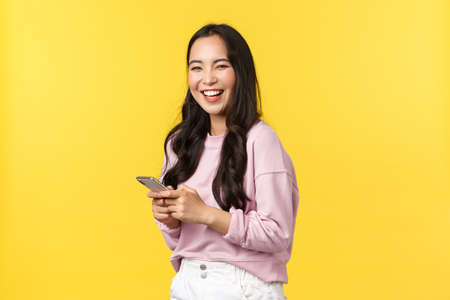 People emotions, lifestyle leisure and beauty concept. Cheerful smiling happy asian woman, turn at camera and laughing after reading funny post on social media app, holding smartphoneの写真素材