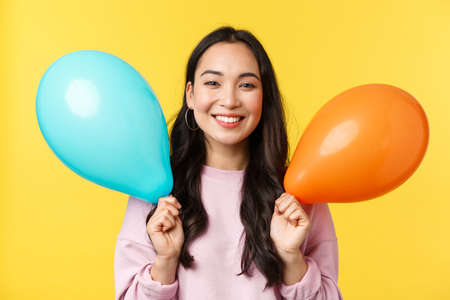 People emotions, lifestyle leisure and beauty concept. Happy cute asian birthday girl celebrating big event, holding balloons congratulating with holidays, standing yellow backgroundの写真素材