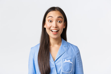 Close-up of enthusiastic and upbeat asian girl in blue pajama looking with thrill at camera. Female...