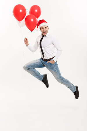 Christmas Concept - Handsome Business man jumping for celebrating merry christmas and happy new year wear santa hat with red balloon.の写真素材