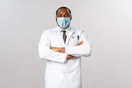 Portrait of proud and confident african-american male doctor in white coat, cross hands chest and smiling pleased, boastful over his nurses and best hospital in town, taking care of patientsの写真素材