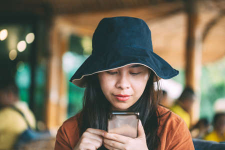 Asian girl sitting in coffee shop playing mobile phone for social media on vacation time, girl relaxing in cafe for holiday, cute girl portraitの写真素材