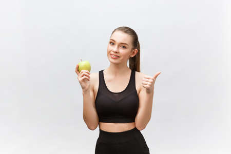 Portrait of a happy young caucasian woman holding and eating green apple over white backgroundの写真素材