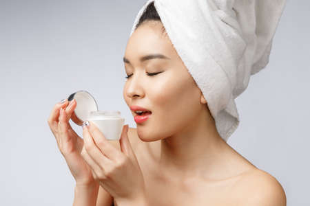 health and beauty concept - Attractive asian woman applying cream on her skin, isolated on white.の写真素材