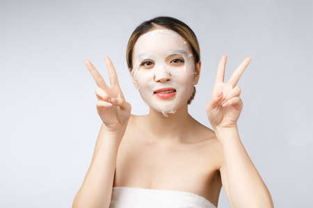 Beautiful asian woman applying paper sheet mask on her face white background.の写真素材
