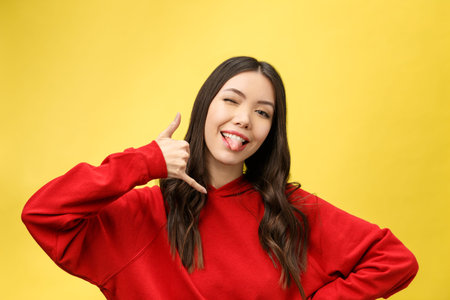 Pretty young woman showing phone sign with her fingers. Colorful studio portrait with yellow...